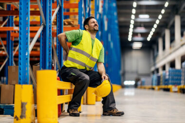 A warehouse worker having back pain and rubbing it.