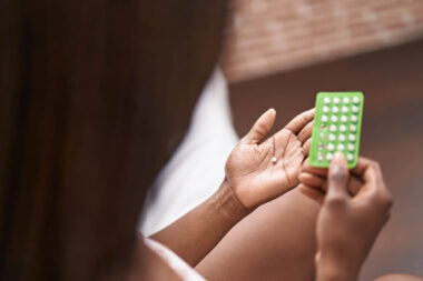 African american woman holding birth control pills sitting on bed at bedroom