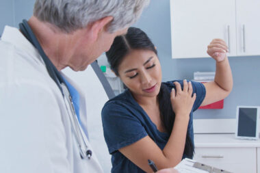 Japanese woman explaining rotator cuff shoulder pain to doctor in exam room