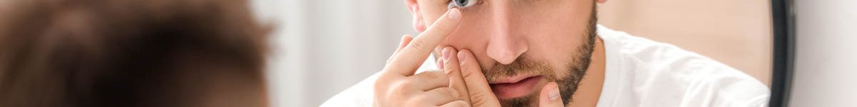 Young man putting in contact lenses near mirror