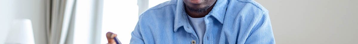 African man is sitting at the sofa and taking blood from his finger due to diabetes. The daily life of a man of African-American ethnicity person with a chronic illness who is using glucose tester.