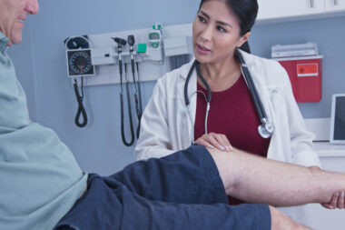Senior man with hurt knee getting it checked by female medical professional