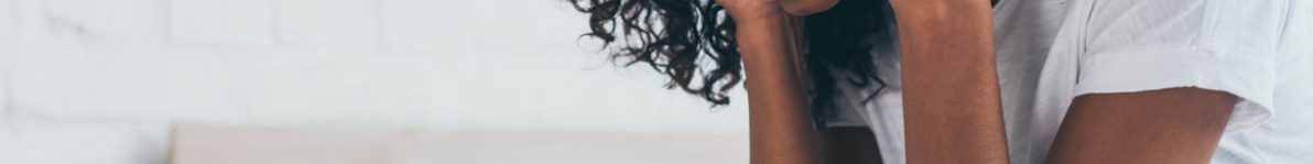 pretty african american woman holding hands near head while suffering from headache in bedroom