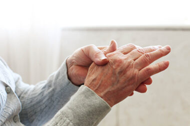 Elderly woman applying moisturizing lotion cream on hand palm, easing aches. Senior old lady experiencing severe arthritis rheumatics pains, massaging, warming up arm. Close up, copy space, background