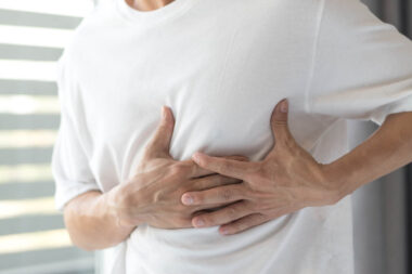 Man’s hands on his chest in white shirt with red spot as sufferi