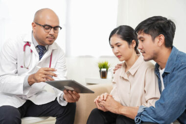 Male doctor giving test result to asian couple patient with tabl