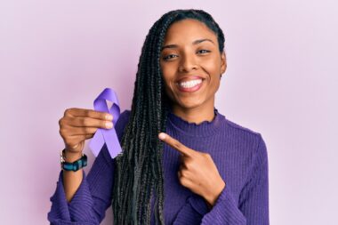 African american woman holding purple ribbon awareness smiling happy pointing with hand and finger